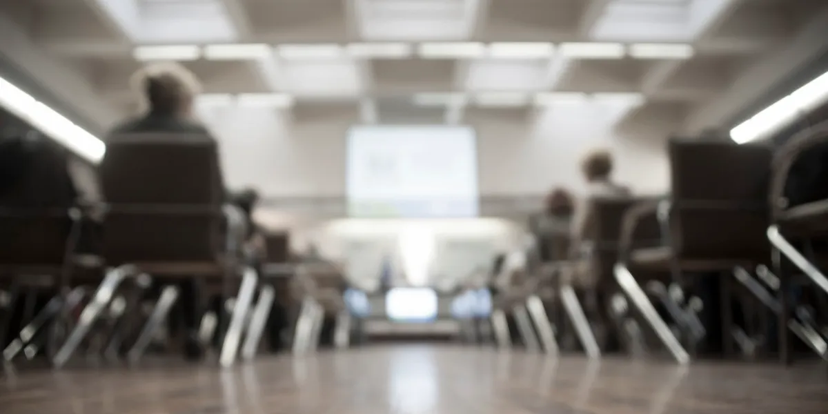 A blurry image of people sitting in chairs at a meeting.
